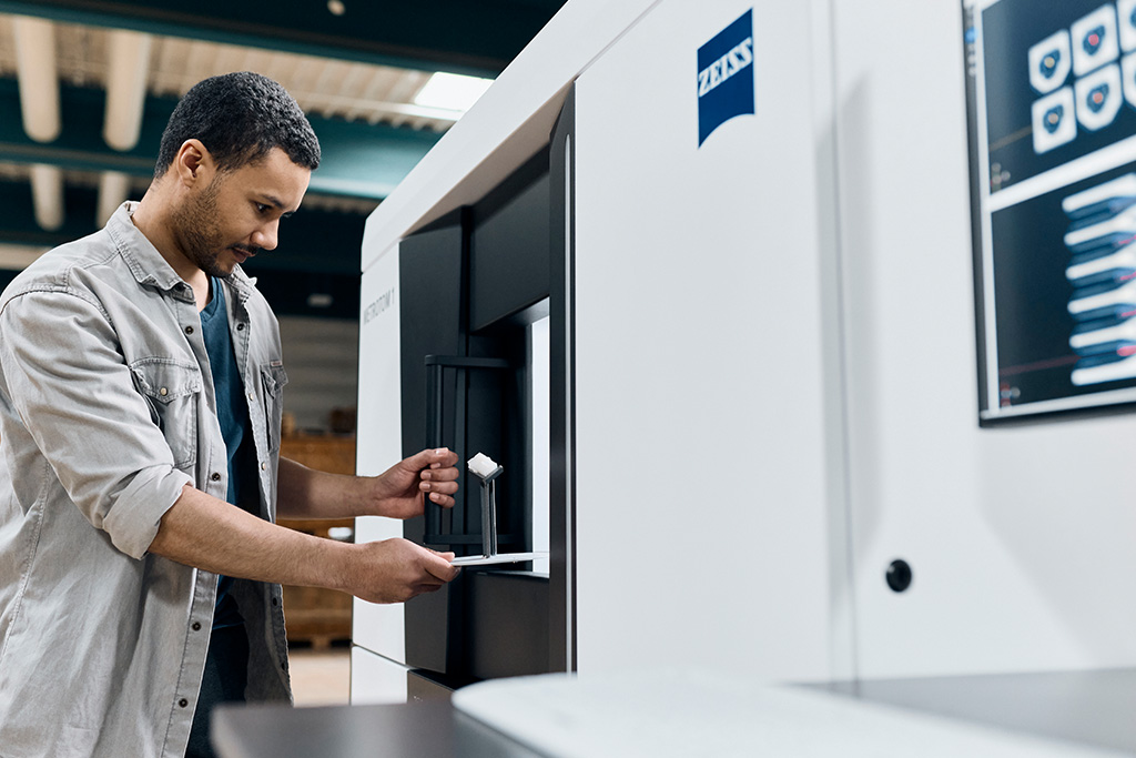 A man placing a white plastic part into a CT scanner