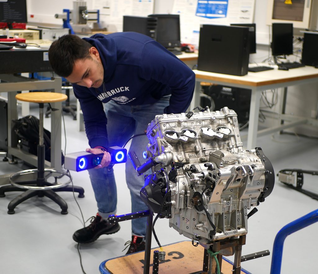 A man using ZEISS T-SCAN hawk 2 to 3D scan a shiny motorcycle component