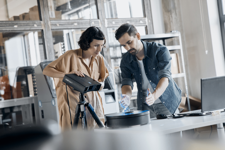 Two people use the industrial 3D scanner GOM Scan 1 to measure a small component on a turntable.